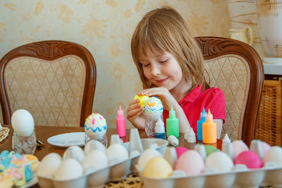Girl making easter eggs while sitting on table at home