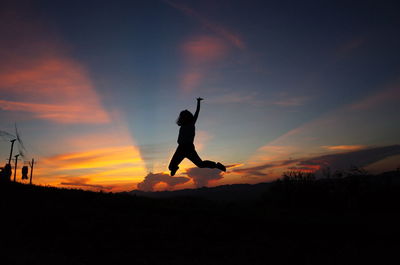 Silhouette girl jumping on field against orange sky during sunset
