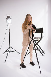 Portrait of young woman holding camera against white background