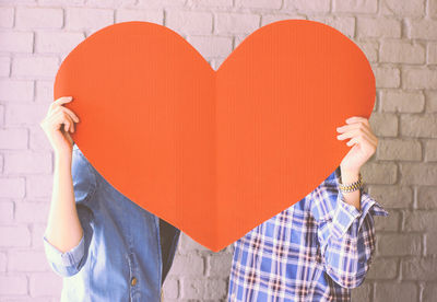 Midsection of couple holding orange heart shaped paper on valentine day