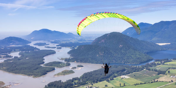 Person paragliding over mountains against sky