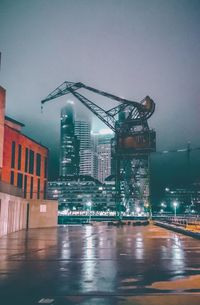 Illuminated buildings by wet city against sky at night