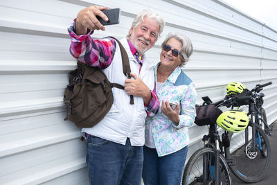 Smiling couple taking selfie while standing by wall outdoors