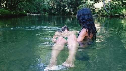 Rear view of two women sitting by lake