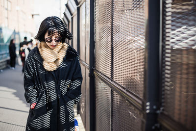 Young woman in warm clothing wearing sunglasses standing by built structure