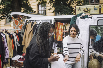 Female owner assisting customer shopping during during second hand sale at flea market