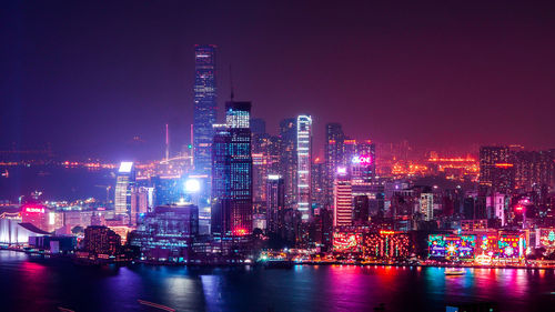 Illuminated buildings by river against sky at night