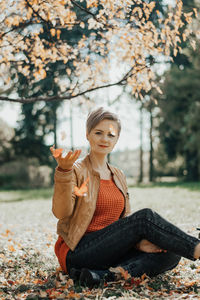 Portrait of young woman sitting on field during autumn