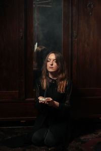 Young woman looking away while sitting on door