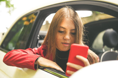 Trendy girl sitting in a car. teen using smartphone and chat with friend. woman enjoying free time 