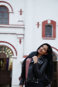 Young woman looking away while standing against built structure