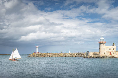 People on a small sailboat exiting howth marina, passing howth lighthouse and per