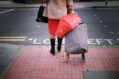 Low section of woman with luggage standing on footpath