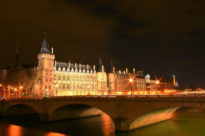 Illuminated bridge over river against buildings at night