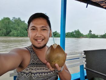 Portrait of smiling man eating food in river against sky