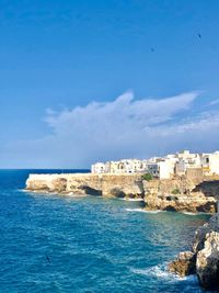 Buildings by sea against blue sky