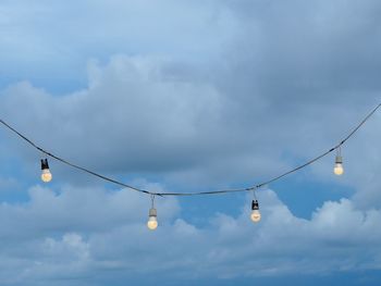 Low angle view of light bulbs hanging against cloudy sky