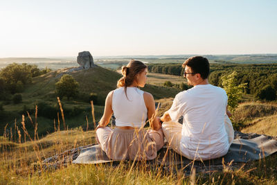 Man and woman practicing yoga and meditation outdoors at sunset with nature miracle giant stone