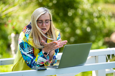 Senior emotional woman with laptop making video call and actively gesturing, online communication