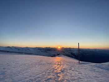 Snow covered field against sky during sunset