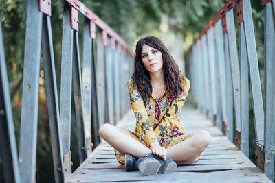 Portrait of young woman sitting on footbridge