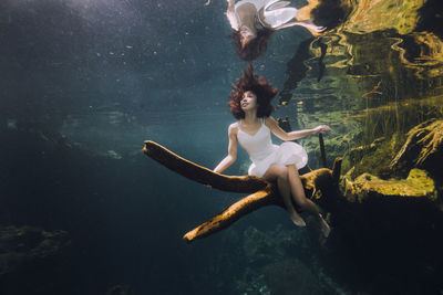 Woman sitting on branch underwater