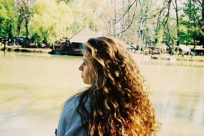 Rear view of woman with long hair at lake against trees