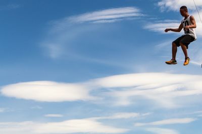 Low angle view of young man jumping against sky