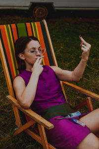 Woman smoking cigarette while showing obscene gesture on chair