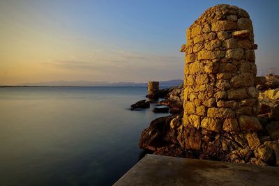 Rock formation by sea against sky during sunset