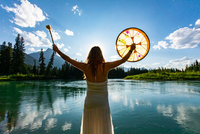 Rear view of woman standing by lake against sky