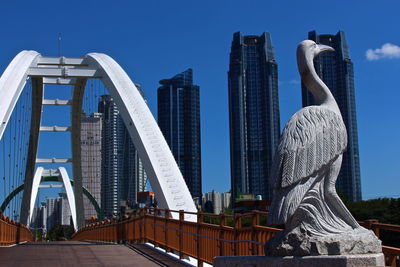 Statue by footbridge against towers in city