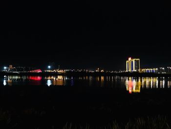 Illuminated buildings by river against sky at night