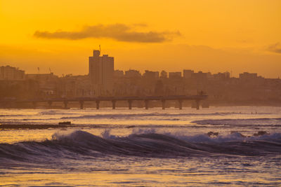 Buildings by sea against sky during sunset