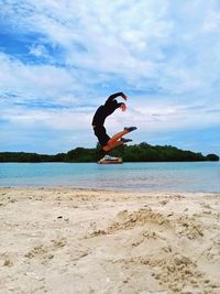 Man jumping at beach against sky
