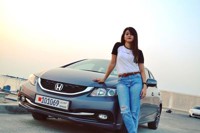 Young woman standing on car against clear sky