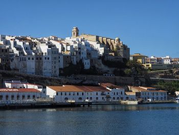 Buildings by river against clear blue sky