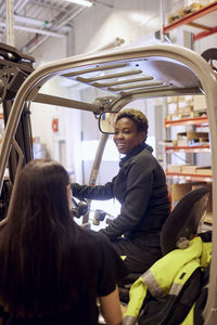 Smiling female forklift operator talking with coworker in distribution warehouse