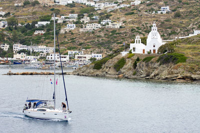 Sailboats in sea by buildings against mountains