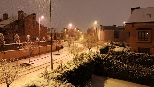 Snow covered street amidst buildings against sky at night