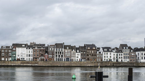 Buildings by river against sky in city