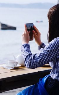 Woman photographing sea through mobile phone