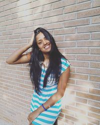 Portrait of young smiling woman standing with hand in hair by wall