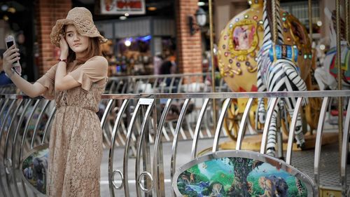 Young woman taking selfie by carousel at amusement park