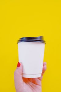 Close-up of hand holding drink against yellow background