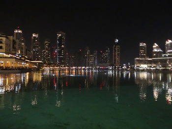 Illuminated city by river against sky at night