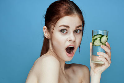 Portrait of woman drinking glass against blue background