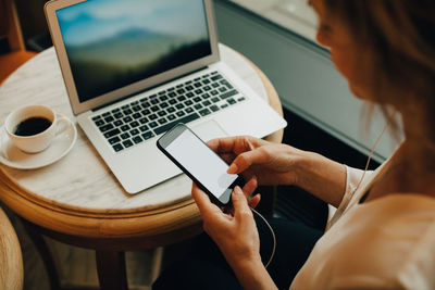 High angle view of businesswoman with laptop on table using mobile phone while sitting in cafe