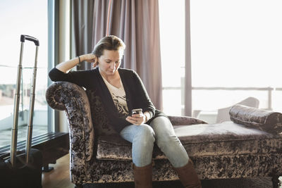 Businesswoman using mobile phone on chaise longue in hotel room