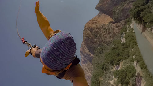 Midsection of woman with arms raised on rock against sky